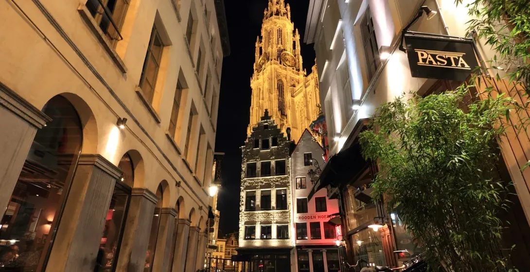 Illuminated Antwerp Cathedral at night, seen from a charming street with restaurants.