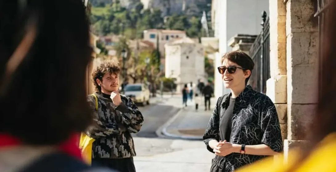 A tour guide leads a small group through the charming streets of Athens, with the Acropolis in the distance.