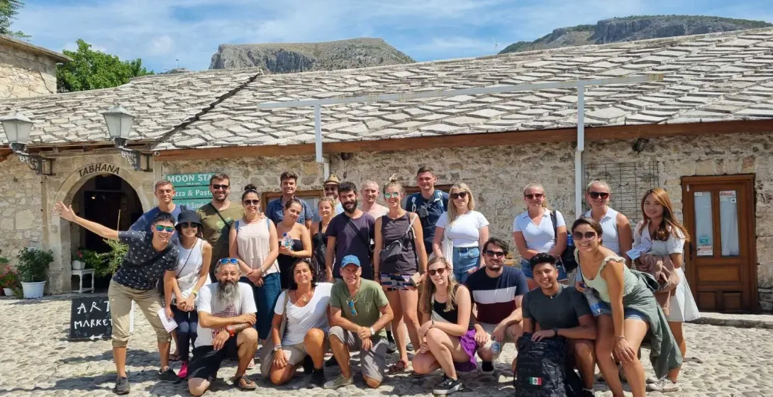 Happy tourists on a group tour in Berat, Albania, posing in front of a historic stone building.