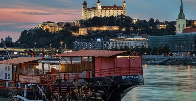 Bratislava Castle at sunset, viewed from a floating bar on the Danube River.