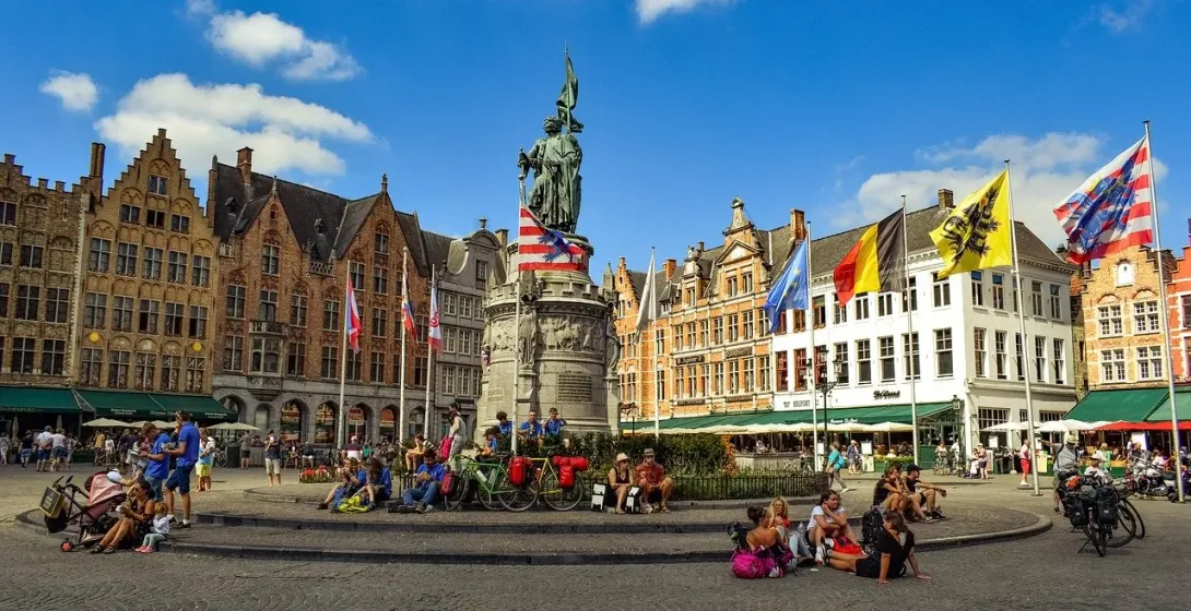 Tourists enjoying the Market Square in Bruges, Belgium, with the Jan van Eyck statue in the background.