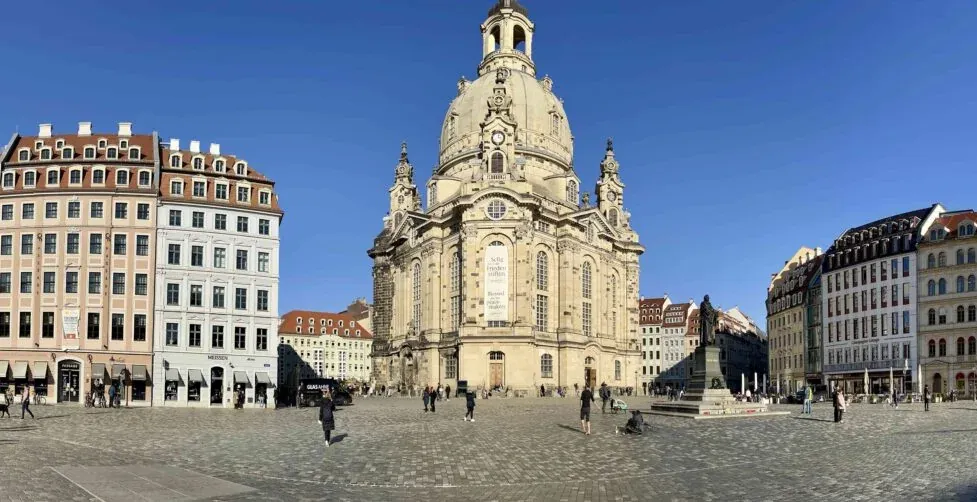 Panoramic view of Dresden's Neumarkt square with the Frauenkirche, surrounded by historic buildings and people walking.