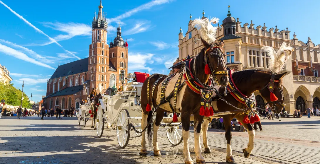 Horse-drawn carriages in Krakow's Main Market Square with St. Mary's Basilica in the background.