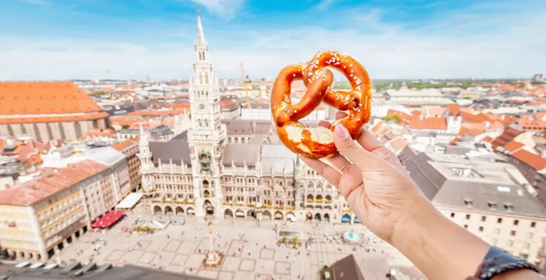 A pretzel held against the backdrop of Munich's Marienplatz.