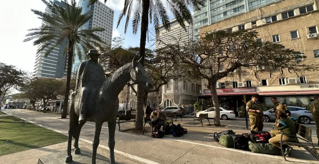 Bronze statue of a man on horseback in Tel Aviv, surrounded by palm trees and modern buildings.