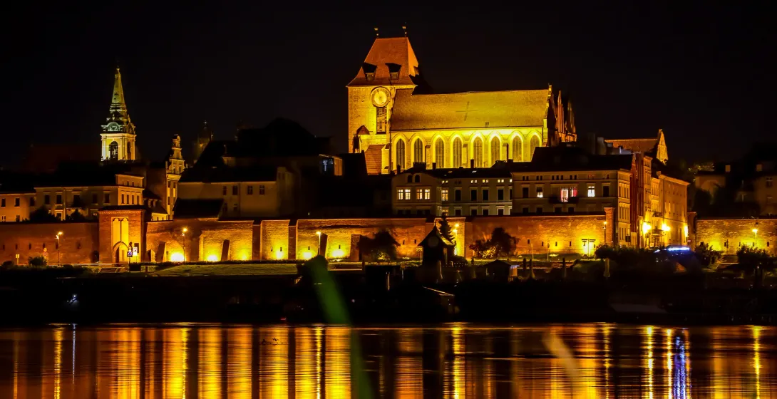 Night view of Toruń's Old Town reflected in the Vistula River.