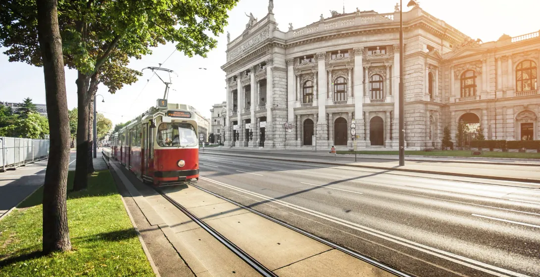 A red tram travels past the Vienna State Opera House.