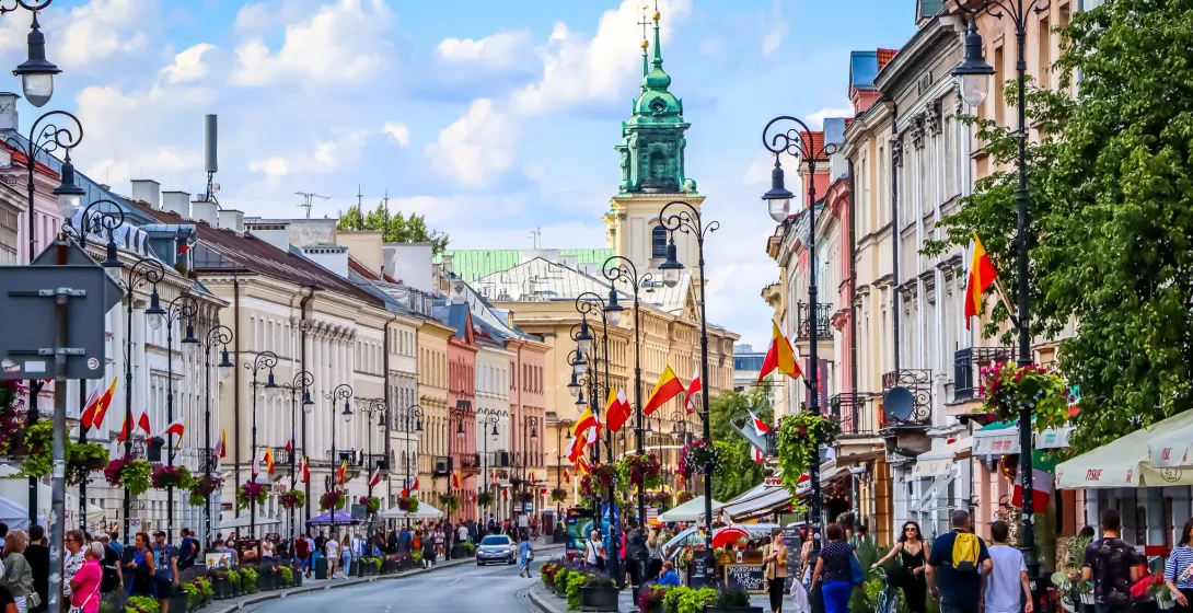 A lively street in Warsaw, Poland, with colorful buildings and many people.
