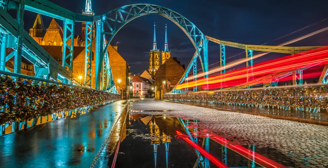 Night view of Tumski Bridge in Wrocław, Poland, with love locks and cathedral in the background.