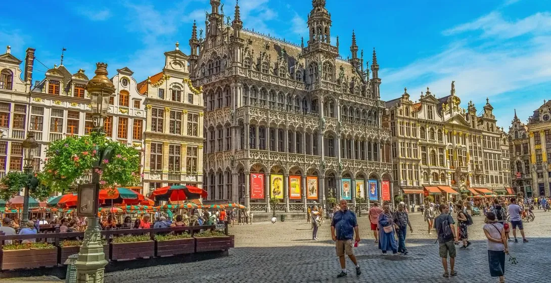 Grand Place in Brussels with ornate historic buildings, outdoor cafes, and people walking on a sunny day.