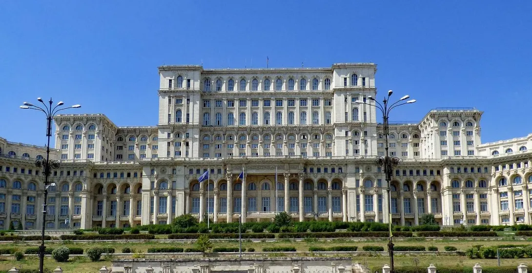 The Palace of the Parliament in Bucharest, a massive white building with many windows and columns, set against a blue sky wit