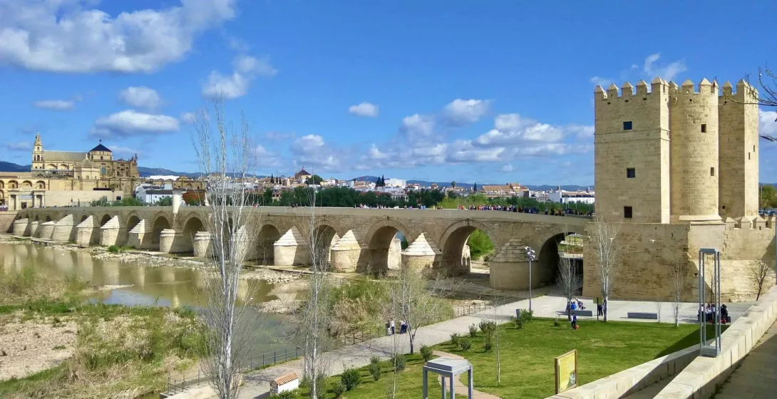 Roman Bridge over Guadalquivir River in Cordoba, with Calahorra Tower and Mezquita-Cathedral in the background under a blue s