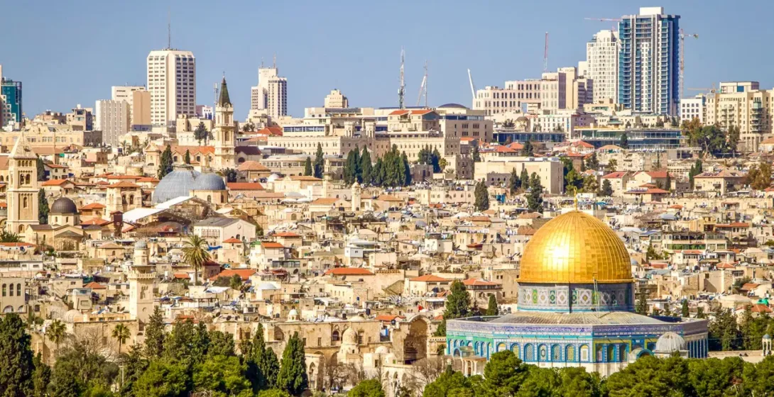 View of Jerusalem with the golden Dome of the Rock in the foreground and the Old City buildings and modern high-rises behind.