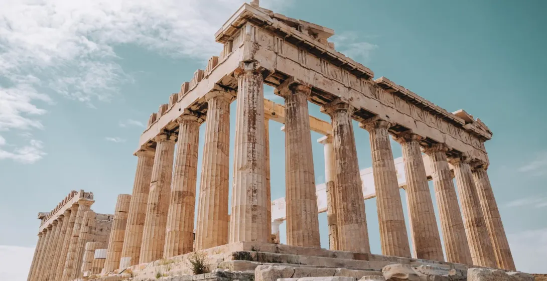 View of the Parthenon temple on the Acropolis in Athens, showing several Doric columns under a partly cloudy sky.