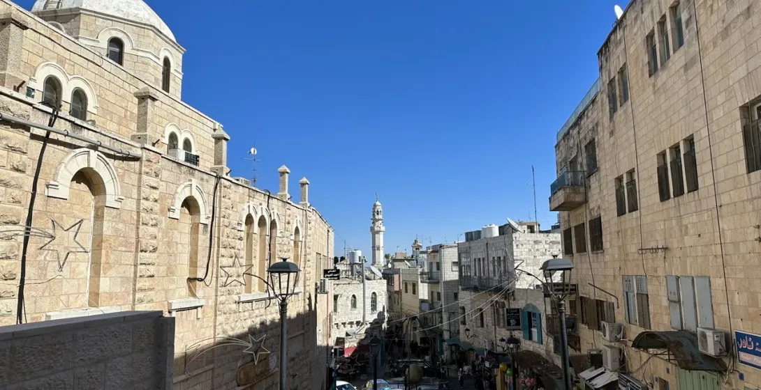 View down a stone street in Bethlehem with a large church building on the left and a distant minaret.