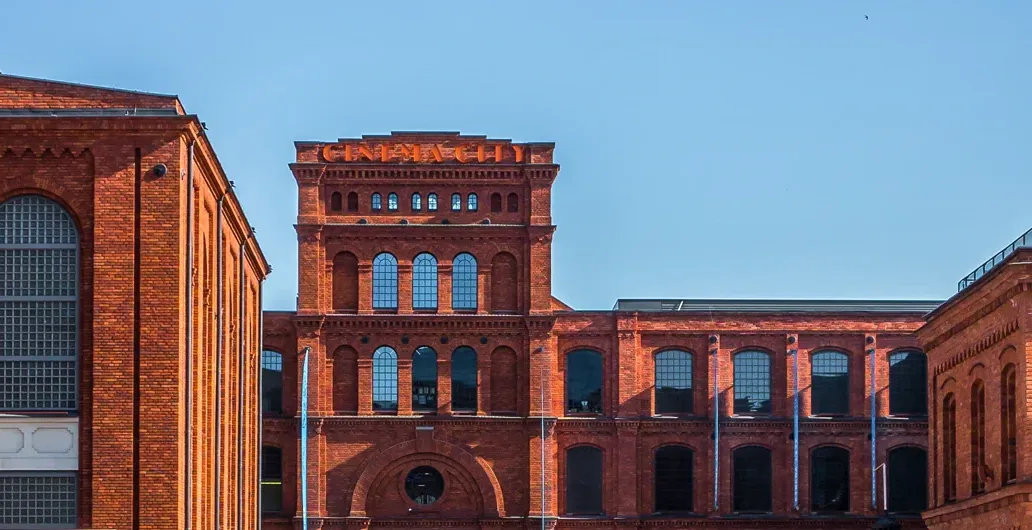 Red brick industrial buildings of Manufaktura with arched windows and a clear blue sky.