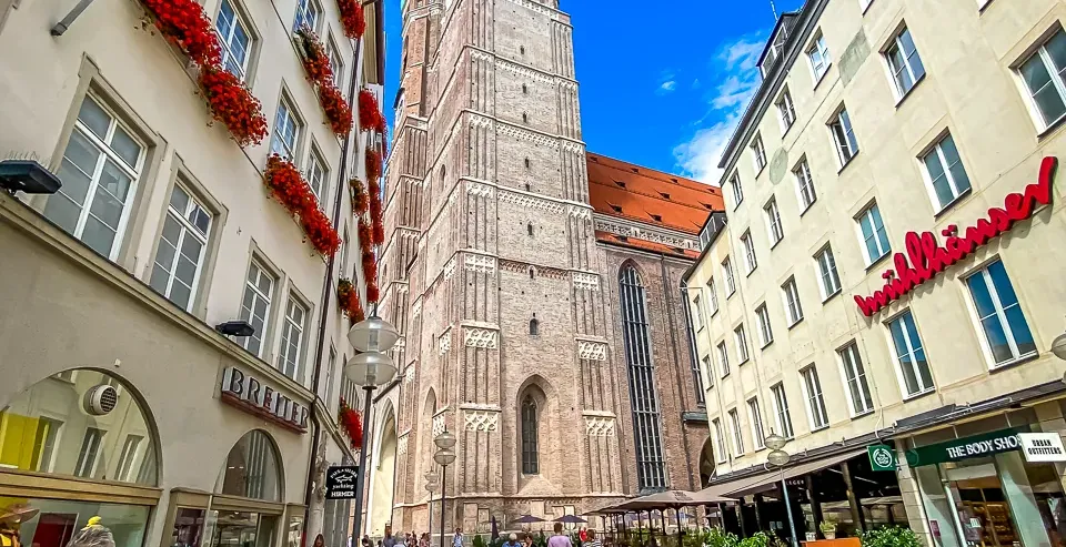 Pedestrian street in Munich with the tall, twin-domed Frauenkirche cathedral in the center, flanked by buildings.