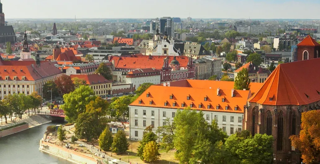 Panoramic aerial view of Wroclaw cityscape with the Odra River, historic buildings with red roofs, church towers, and lush gr
