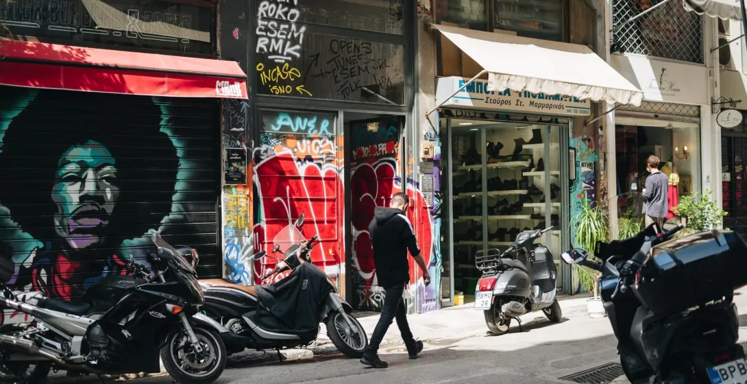 A vibrant street scene in Athens, Greece, featuring colorful graffiti and parked scooters.