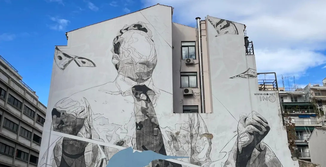 A large grayscale mural of an abstract figure adorns a building in Athens, Greece.
