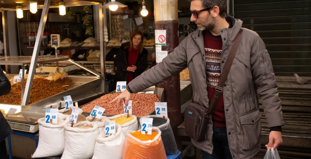 A tour guide shows tourists various legumes and nuts at a vibrant market in Athens, Greece.
