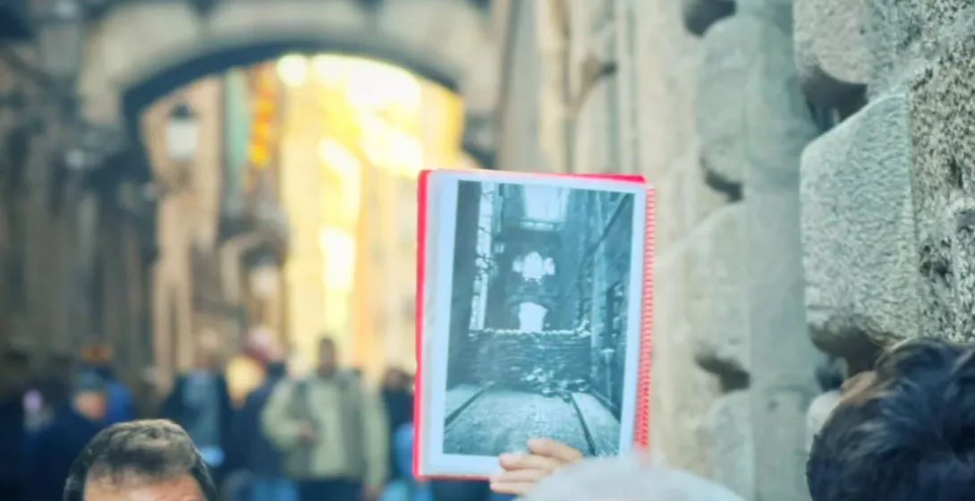 A tour guide in Barcelona's Gothic Quarter shows a historical photo to a group.