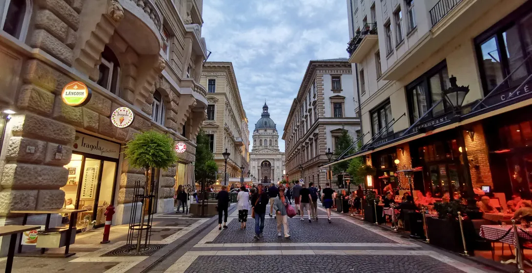 Tourists walking down a charming cobblestone street in Budapest, Hungary, with St. Stephen's Basilica in the background.