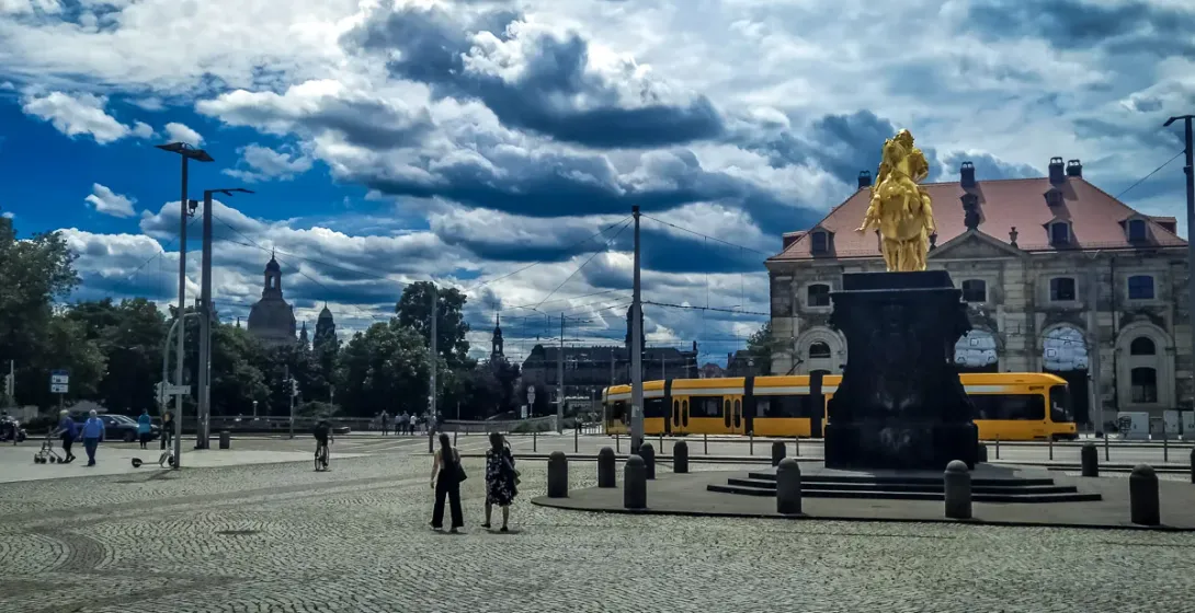 The Golden Horseman statue in Dresden's cobblestone square, with a tram and city skyline in the background.