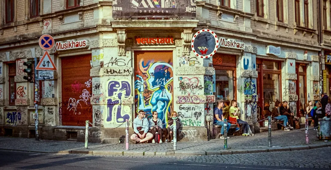 A vibrant street scene in Dresden Neustadt, showcasing graffiti art and a group of people enjoying the atmosphere.