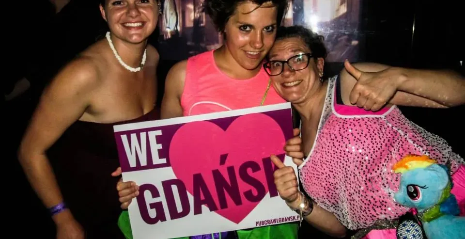 Three happy tourists in Gdańsk, Poland, holding a sign that says 'We ❤ Gdańsk'.