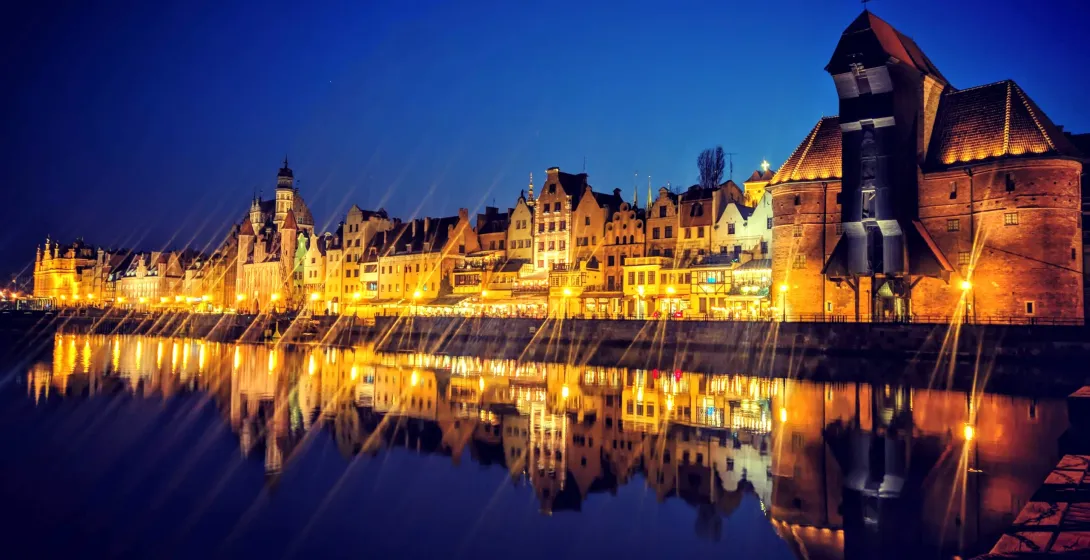 Gdansk's illuminated waterfront at night, reflected in the water. Free Walkative! Tour.