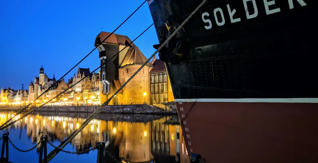 Evening view of Gdansk's Old Town reflected in the Motława River, with the historic ship Soldek in the foreground.