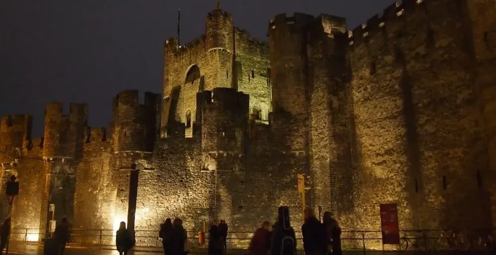Tourists admiring Gravensteen Castle in Ghent at night.