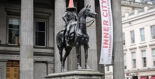 Equestrian statue of the Duke of Wellington in Glasgow city center, wearing an orange traffic cone on its head, in front o...