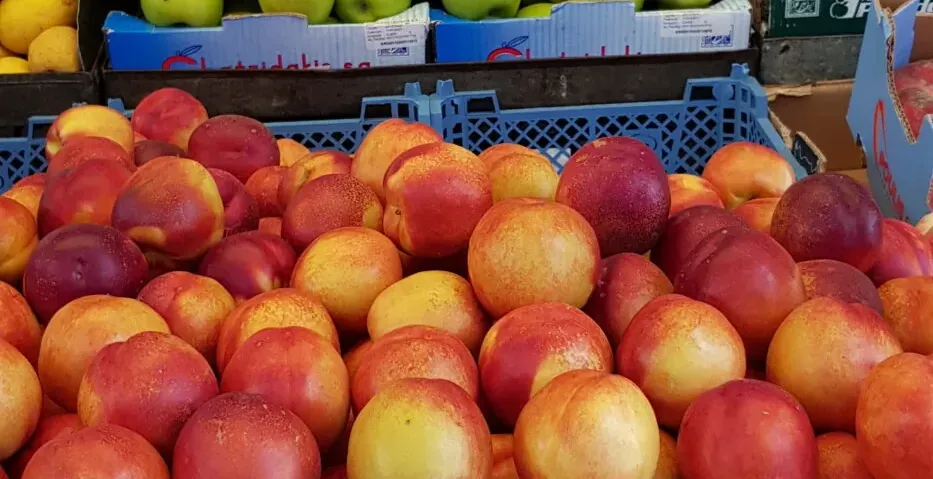 A colorful fruit stand in a Greek market, brimming with fresh apples, oranges, and peaches.