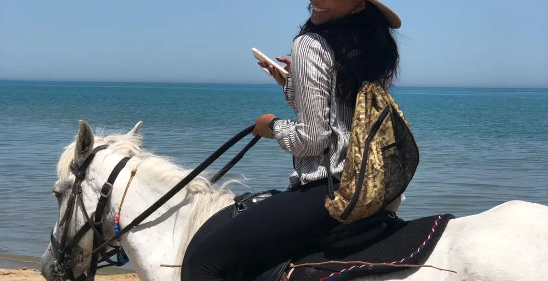 Woman enjoying a horseback riding tour on a beautiful beach.