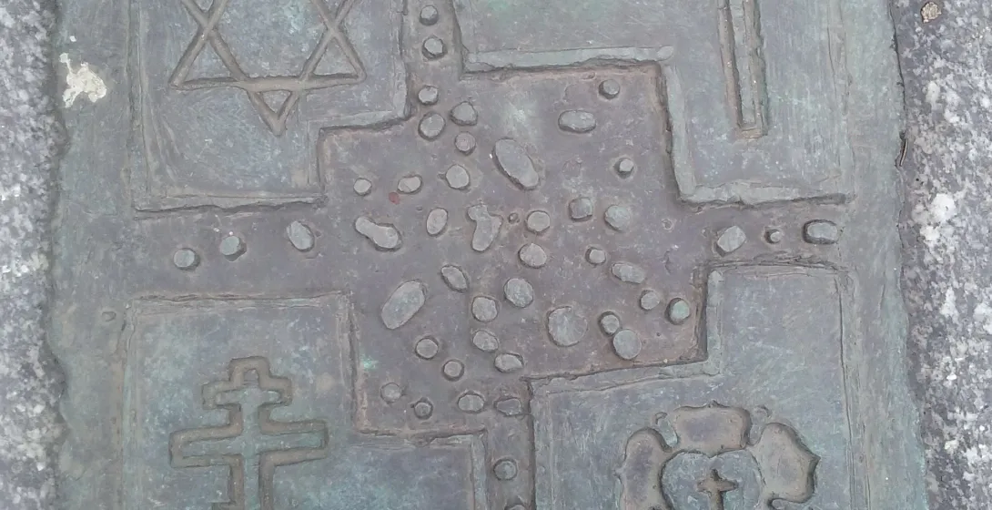 Bronze plaque depicting four religious symbols: Star of David, Christian cross, Orthodox cross, and a heart with a cross.