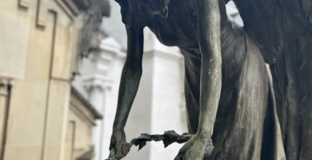 A bronze angel sculpture in Krakow's Rakowicki Cemetery, placing a wreath on a figure.