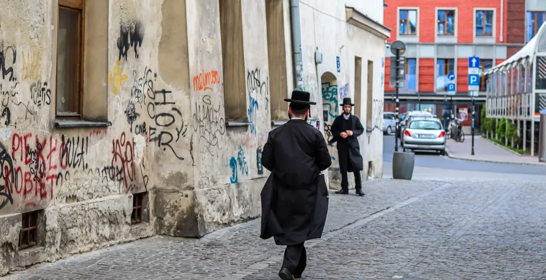 Two men in traditional clothing walk down a cobblestone street in Krakow's Kazimierz district.
