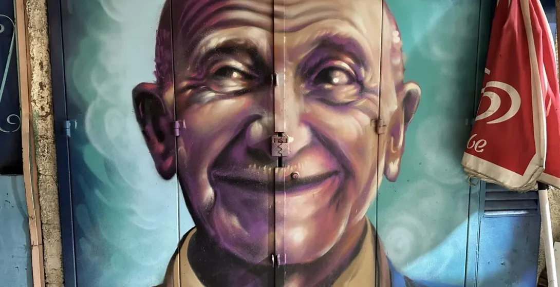 Vibrant street art mural of a smiling elderly man in Lisbon, Portugal.