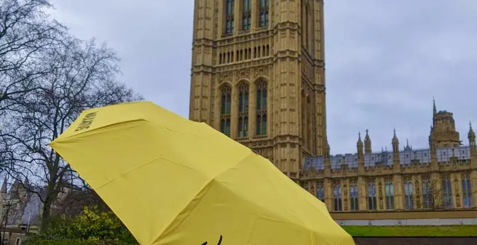 Yellow umbrella with 'Walkative!' logo in front of the Palace of Westminster, London.