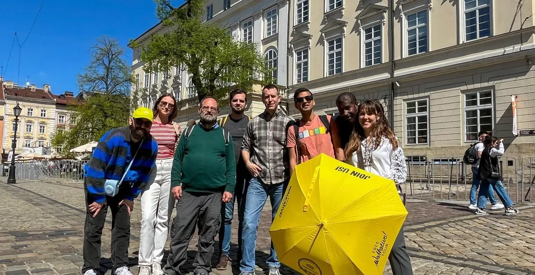 A diverse group of seven people on a cobblestone street in Lviv, with a guide holding a yellow Walkative umbrella in front...