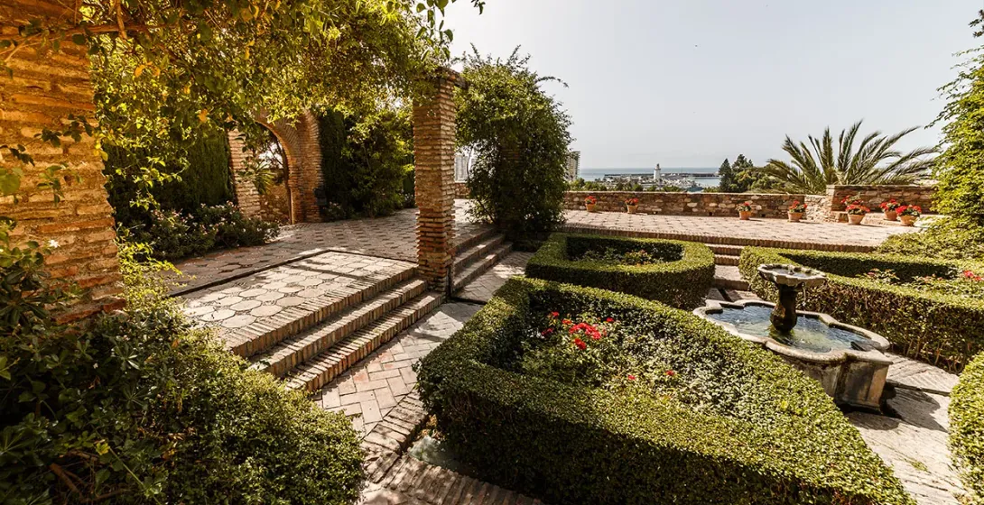 Serene garden in Málaga, Spain, with a fountain and coastal views.