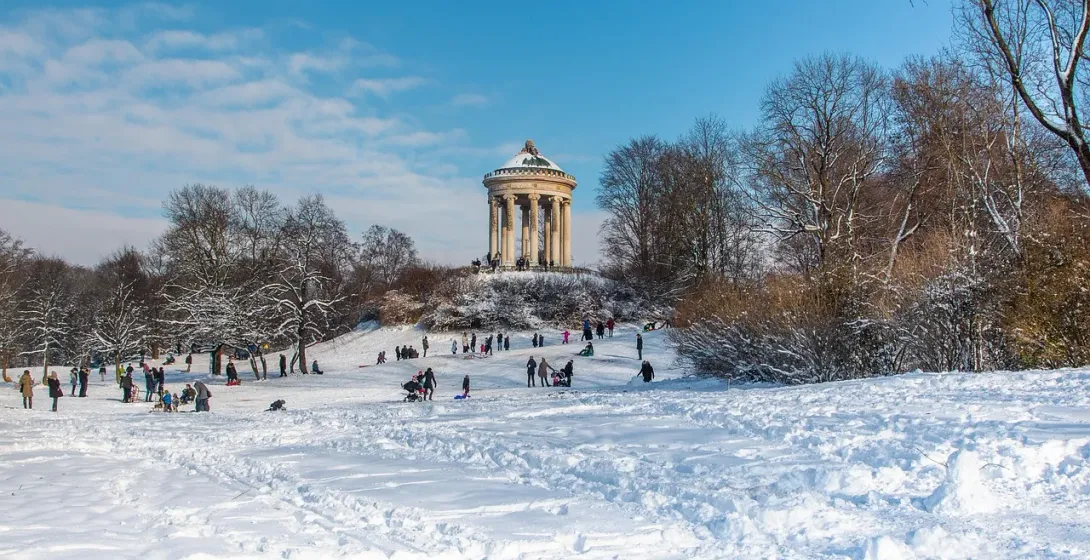 Snow-covered Englischer Garten in Munich with the Monopteros temple and people sledding.