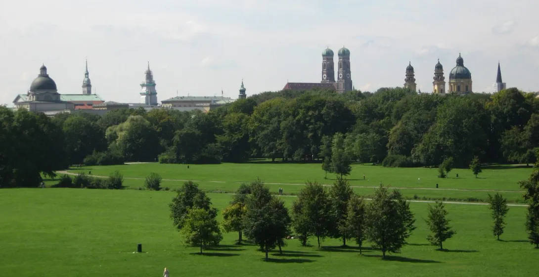 Panoramic view of a green park in Munich, Germany, with the city's skyline visible in the background.