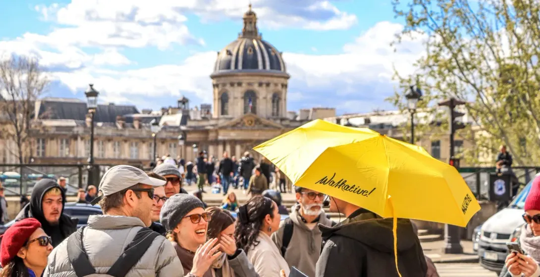 A Walkative! tour guide leads a group of happy tourists on a sunny day in Paris.