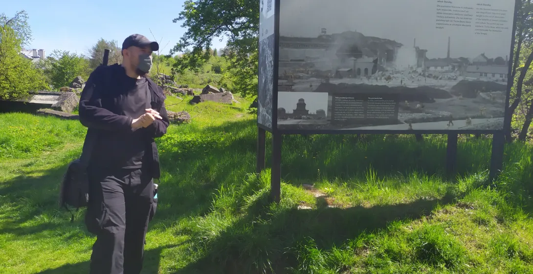 A tourist explores a historical site in Poland, reading an information board with historical photos.