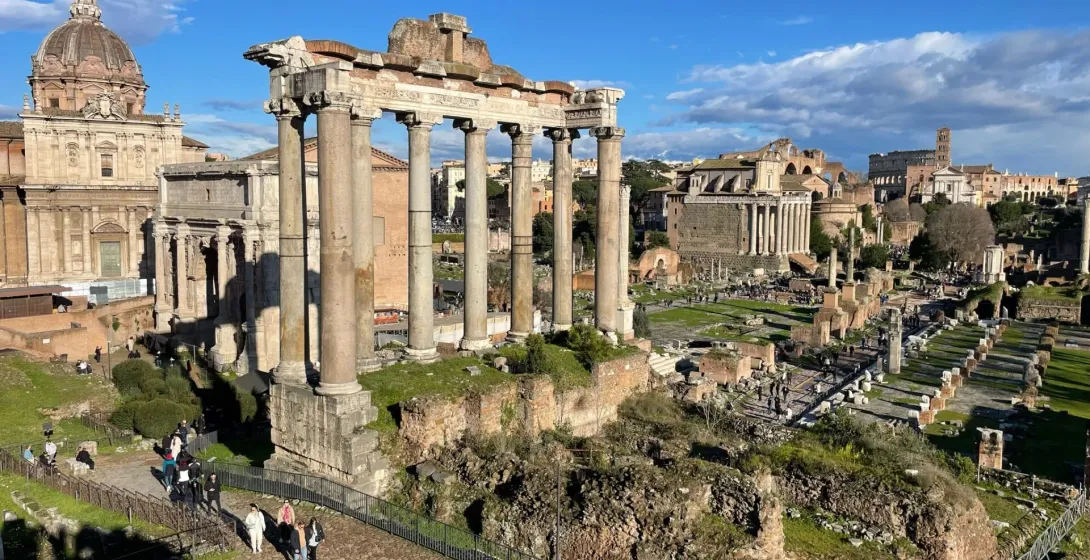 Panoramic view of the Roman Forum in Rome, Italy, with tourists exploring the ancient ruins.
