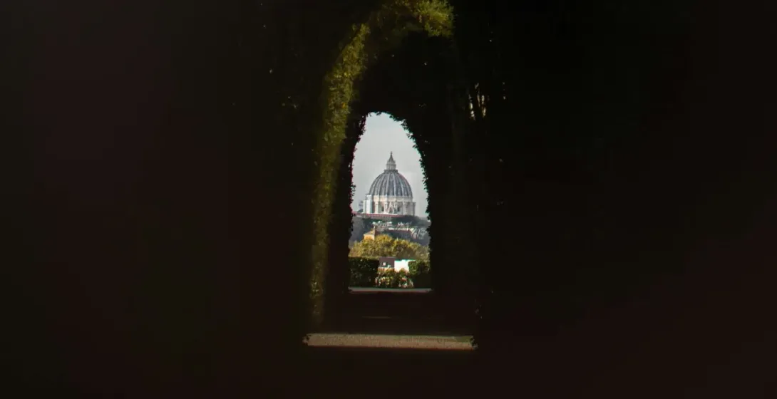 St. Peter's Basilica in Rome, seen through a hedge archway.