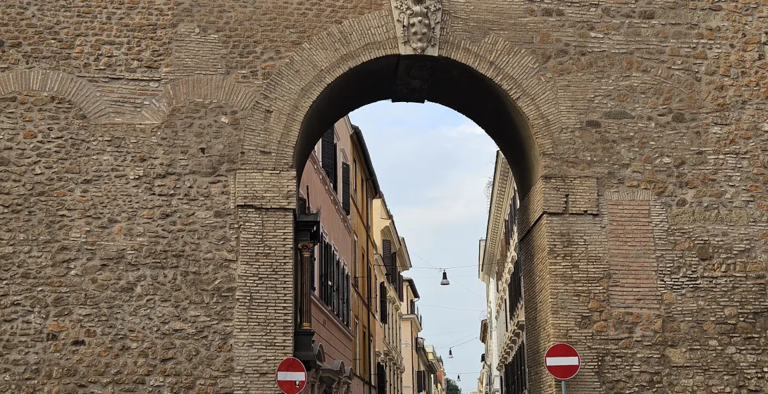 Ancient Roman archway in Rome, offering a glimpse of a charming street.